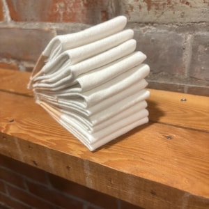 May include: A stack of white cotton tea towels folded neatly on a wooden surface.