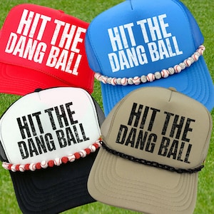 May include: Four baseball-themed trucker hats in red, blue, white, and tan. Each hat features the text "HIT THE DANG BALL" in bold white or black lettering. The blue and white hats have baseball-themed trim.