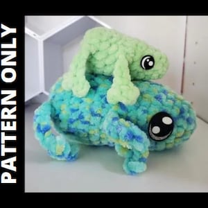 May include: Two crocheted stuffed green and blue frogs. The smaller frog is sitting on top of the larger frog. Both frogs have large black eyes.