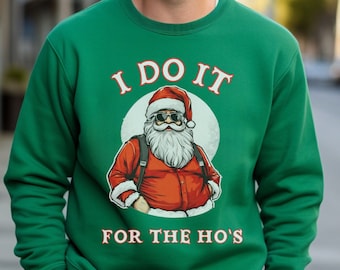 May include: A green sweatshirt with the text "I DO IT FOR THE HO'S" and a graphic of Santa Claus wearing sunglasses. The Santa graphic is in a circle with a white background. The person in the image is smiling.