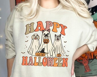 May include: A beige crewneck sweatshirt featuring a graphic print of three dogs dressed as ghosts for Halloween. The text "HAPPY HALLOWEEN" appears in retro-style orange and brown lettering above and below the dogs, accompanied by small pumpkins and bats.