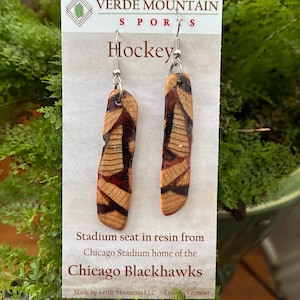 May include: Hockey earrings made from stadium seat resin. The earrings are rectangular with a natural wood grain pattern and dark red accents. The text on the card reads "VERDE MOUNTAIN SPORTS" and "Hockey". The earrings are from the Chicago Blackhawks.