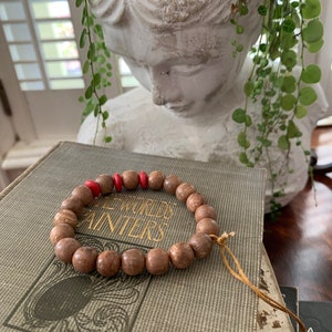 May include: A brown wooden beaded bracelet with two red beads. The bracelet is on a book with the text "The Worlds Painters Hoyt" on the cover.