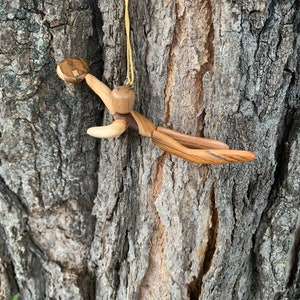 May include: A wooden figurine of a person skydiving, hanging from a yellow cord. The figurine is made of light and dark wood, with details carved into the wood.