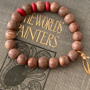 May include: A wooden beaded bracelet with red accents. The bracelet is made of dark brown wood beads and has a simple design. The beads are round and smooth, and the bracelet is tied with a thin string.