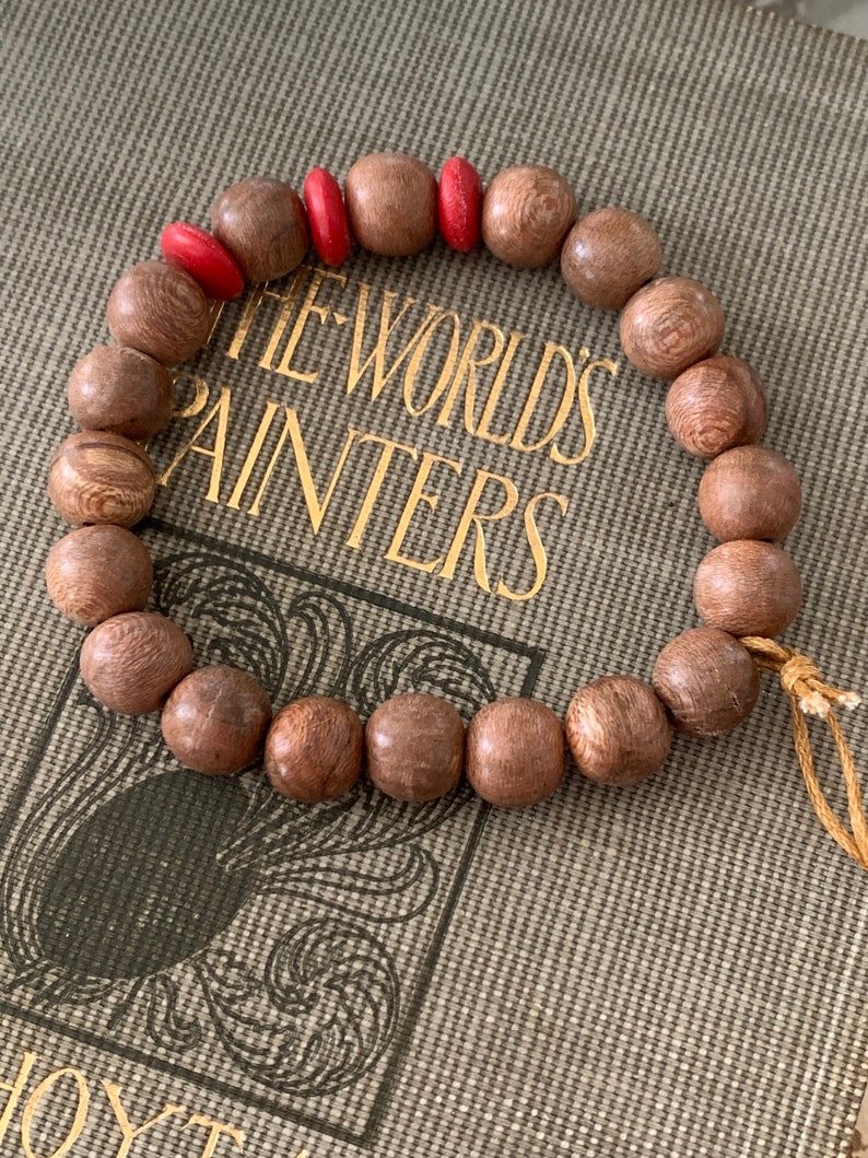 May include: A wooden beaded bracelet with red accents. The bracelet is made of dark brown wood beads and has a simple design. The beads are round and smooth, and the bracelet is tied with a thin string.