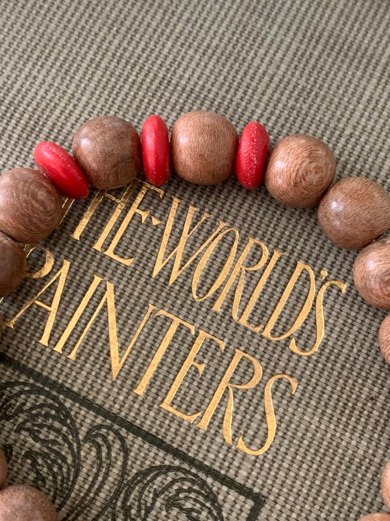 May include: A wooden bracelet with red beads. The bracelet is on a book with the words "The World's Painters" on the cover.