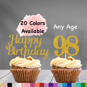 May include: Two cupcakes with gold glitter cake toppers. One topper says "Happy Birthday" and the other says "98". The cupcakes are on a wooden surface. 20 Colors Available. Any Age.