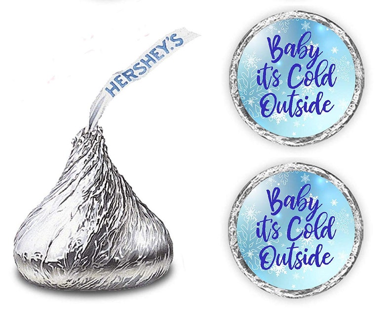 May include: Two blue and silver round stickers with the text "Baby it's Cold Outside" in blue cursive font. The stickers are decorated with white snowflakes. The stickers are designed to be placed on Hershey's Kisses chocolate candies.