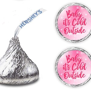 May include: Two pink and white round stickers with the text "Baby it's Cold Outside" in white and pink lettering. The stickers are designed to be placed on Hershey's Kisses chocolate candies.
