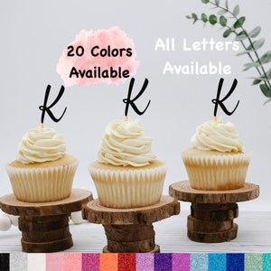 May include: Three cupcakes with white frosting and black letter K toppers. The cupcakes are on wooden cake stands. The text "20 Colors Available" and "All Letters Available" is written on the image.