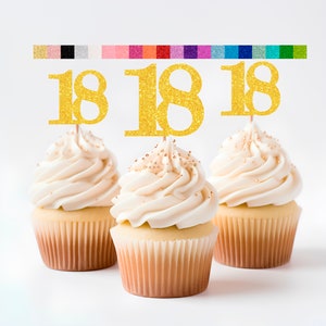 May include: Three cupcakes with white frosting and gold sprinkles topped with gold glitter "18" cupcake toppers.