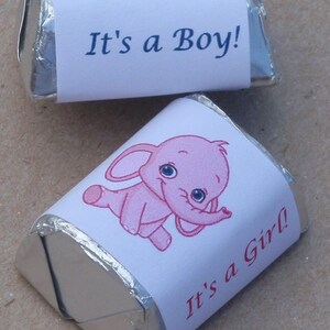 May include: Two silver foil-wrapped chocolate candies with printed labels. One label features a blue elephant with the text "It's a Boy!" and the other label features a pink elephant with the text "It's a Girl!"