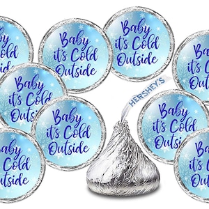 May include: A set of 10 blue and silver round stickers with the text "Baby it's Cold Outside" printed in purple. The stickers are designed to be placed on Hershey's Kisses chocolate candies.