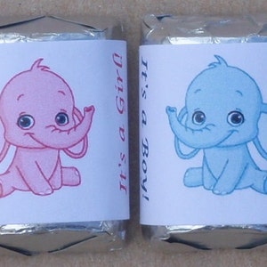 May include: Two chocolate bar wrappers with a baby elephant design. One wrapper is pink with the text "It's a Girl!" and the other is blue with the text "It's a Boy!"