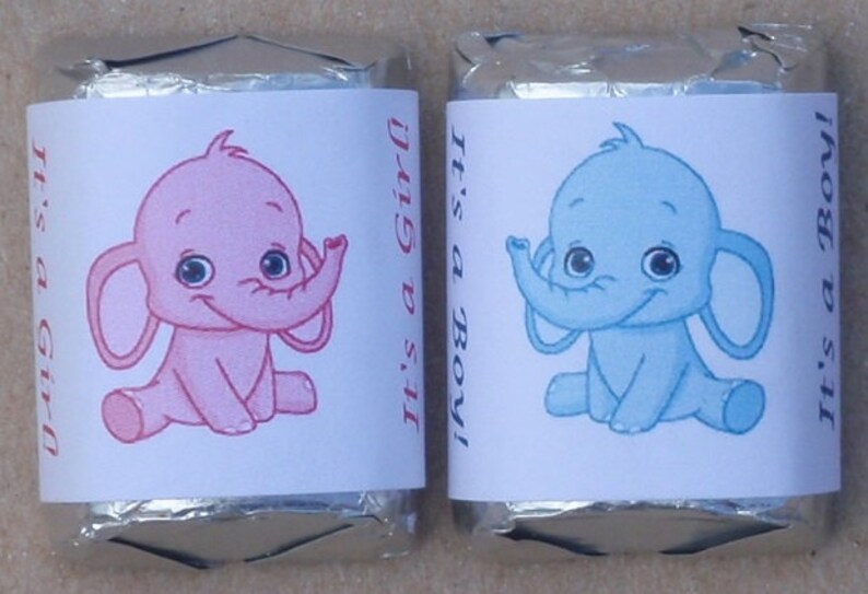 May include: Two chocolate bar wrappers with a baby elephant design. One wrapper is pink with the text "It's a Girl!" and the other is blue with the text "It's a Boy!"