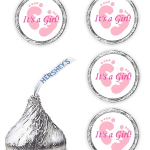 May include: Four white round stickers with pink baby footprints and the text "It's a Girl!" printed in pink. The stickers are designed to be placed on Hershey's Kisses chocolate.