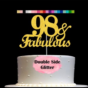 May include: Gold glitter cake topper with the numbers 98 and the word "fabulous" in a cursive font. The topper is on a white cake with the words "Double Side Glitter" printed on the side.