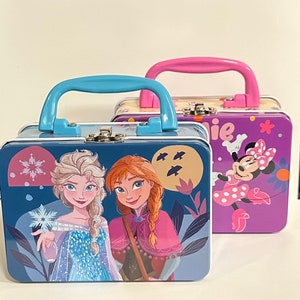 May include: Two metal lunch boxes with carrying handles. The blue lunch box features a design of Elsa and Anna from Frozen. The purple lunch box features a design of Minnie Mouse.