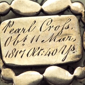 May include: A silver brooch with a pearl design and an inscription that reads "Pearl Cross, Ob: 4 11 - Morn, 1817 Oct: 40 Yrs."