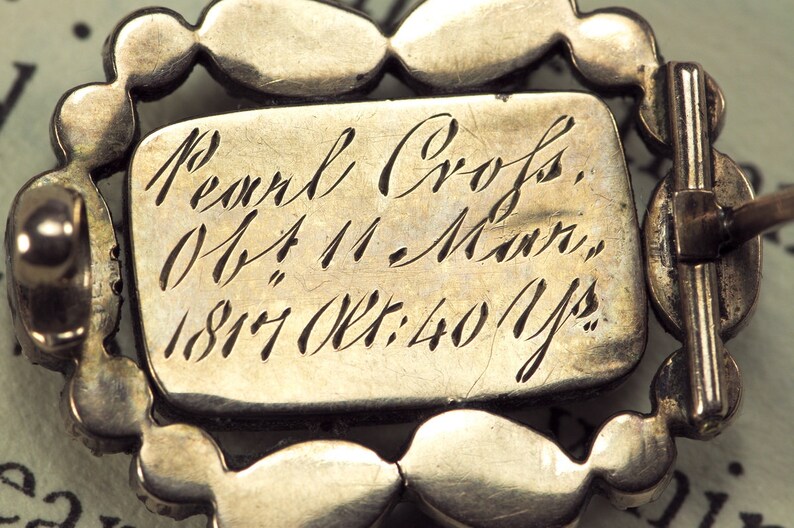 May include: A silver brooch with a pearl design and an inscription that reads "Pearl Cross, Ob: 4 11 - Morn, 1817 Oct: 40 Yrs."