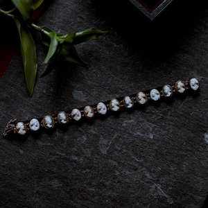 May include: A vintage bracelet with oval cameo portraits in gold-tone settings. The cameos are white with brown details, set on a black band. The bracelet is displayed on a dark, textured surface.