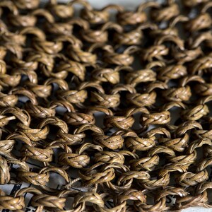 May include: Close-up of a woven chainmail made of brown leather. The chainmail is made of small, interlocked rings.