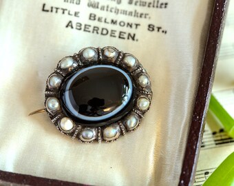 May include: A silver brooch with a black and white agate stone surrounded by a ring of pearls.