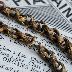 May include: A close-up of a woven chain made of brown material. The chain is lying on top of a piece of paper with text that reads "Class 2 &pound;20 Class 4 &pound;23 Class 5 &pound;25 Best" and "RICAN ORGANS".