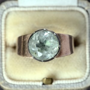 May include: A silver ring with a large, faceted, light green gemstone set in a bezel setting.