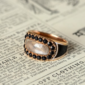 May include: A gold ring with a black enamel band and a clear oval locket set with black gemstones. The locket contains a lock of hair.
