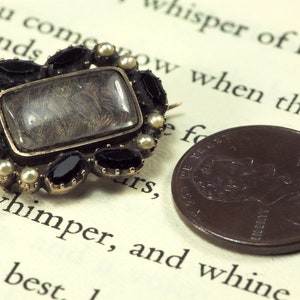 May include: A gold-toned locket with a glass window containing a lock of hair. The locket is surrounded by black and white gemstones.