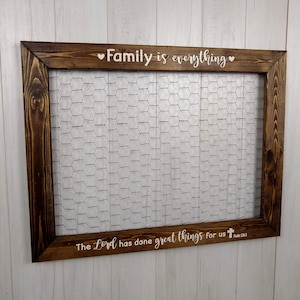 May include: A brown wooden frame with a wire mesh insert. The frame has the text "Family is everything" with a heart on each side. The bottom of the frame has the text "The Lord has done great things for us" with a cross and the reference "Psalm 126:3".