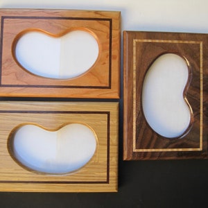 May include: Four wooden picture frames with kidney-shaped openings. The frames are made of different types of wood, including light and dark tones, and feature decorative borders. The frames are designed to hold photos or artwork.
