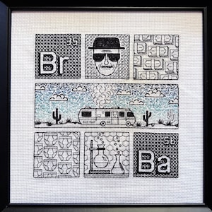 Peut inclure: Broderie au point de croix noir et blanc dans un cadre noir. La broderie représente une scène de la série télévisée Breaking Bad, avec les personnages Walter White et Jesse Pinkman, le camping-car et les éléments chimiques Br et Ba.