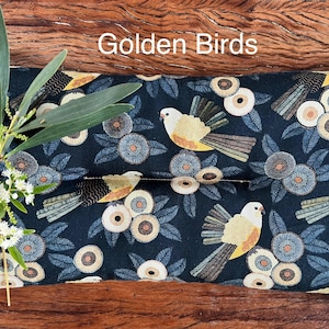 May include: A rectangular tissue box cover with a dark blue background featuring a pattern of stylized birds and floral elements in shades of yellow, beige, and blue. The text "Golden Birds" is displayed at the top.