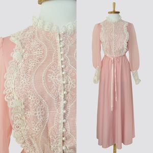 Könnte beinhalten: Ein langärmeliges rosa Kleid mit einer weißen Spitzenüberlage und Perlenknöpfen. Das Kleid hat einen hohen Ausschnitt und ein tailliertes Oberteil. Der Rock ist weit und fließend.