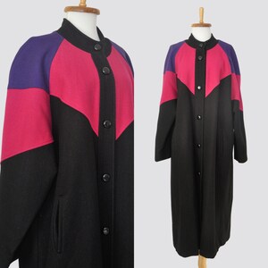 May include: A long black wool coat with a pink and purple color block design. The coat has a button-up front and long sleeves.