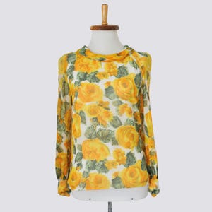 May include: A sheer, long-sleeved blouse with a white background and a yellow floral print. The flowers are large and have a yellow centre with green leaves.