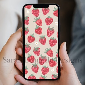 May include: A smartphone displaying a digital wallpaper with a pattern of red strawberries and white flowers on a beige background.