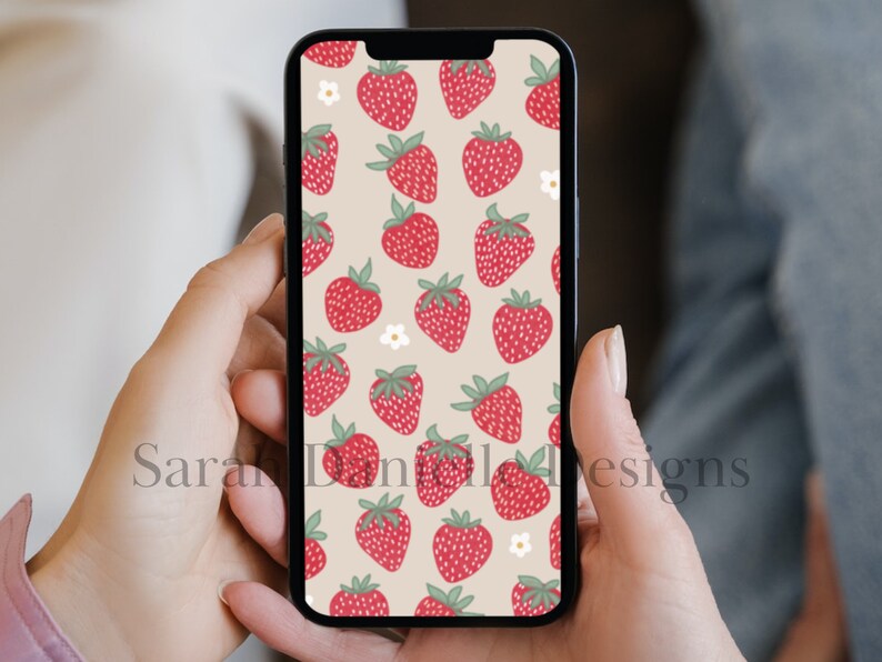 May include: A smartphone displaying a digital wallpaper with a pattern of red strawberries and white flowers on a beige background.