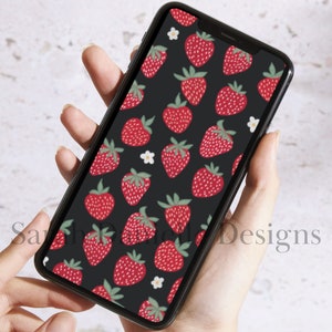 May include: A black phone case with a pattern of red strawberries and white flowers. The phone case is being held in a person's hand.