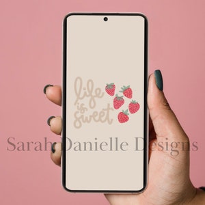 May include: A beige phone screen with the text "life is sweet" in brown script. There are five red strawberries with green leaves on the screen.
