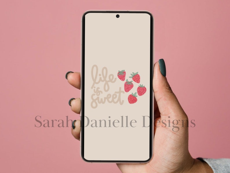 May include: A beige phone screen with the text "life is sweet" in brown script. There are five red strawberries with green leaves on the screen.