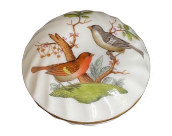 May include: A white porcelain trinket box with a scalloped lid. The lid features a hand-painted design of two birds perched on a branch with green leaves and pink flowers.