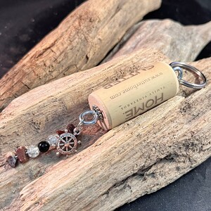 May include: A cork keychain with a silver charm and beads. The cork is engraved with "HOME" and "Family Vineyards" and the website "www.sutterhome.com".
