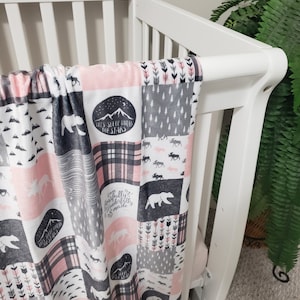May include: A pink and grey baby blanket with a patchwork design featuring bears, moose, arrows, and mountains. The blanket has the text "Let's sleep under the stars" and "I am fearfully and wonderfully made".
