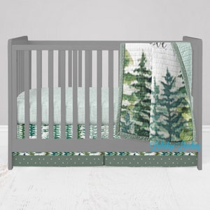 May include: A gray crib with a green and white patterned crib bedding set. The bedding includes a quilt, fitted sheet, and a crib skirt. The quilt features a woodland design with trees and leaves.