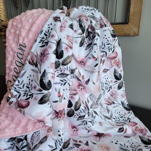 May include: A pink and white baby blanket with a floral pattern. The blanket is personalised with the name "Megan" in pink embroidery.