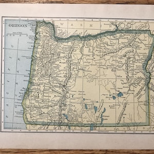 Puede incluir: Un mapa vintage de Oregón, que muestra las fronteras del estado, las principales ciudades y los ríos. El mapa está impreso en blanco y negro con acentos azules y verdes. El mapa está titulado "Oregón" e incluye una barra de escala y una rosa de los vientos.